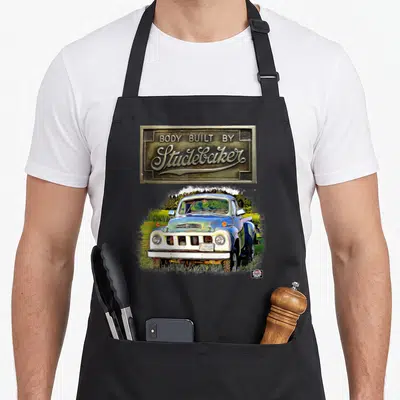 Studebaker truck apron - Brass emblem reading Body Built By Studebaker above blue and white vintage pickup in grass — shown on a black cotton canvas apron against a white background