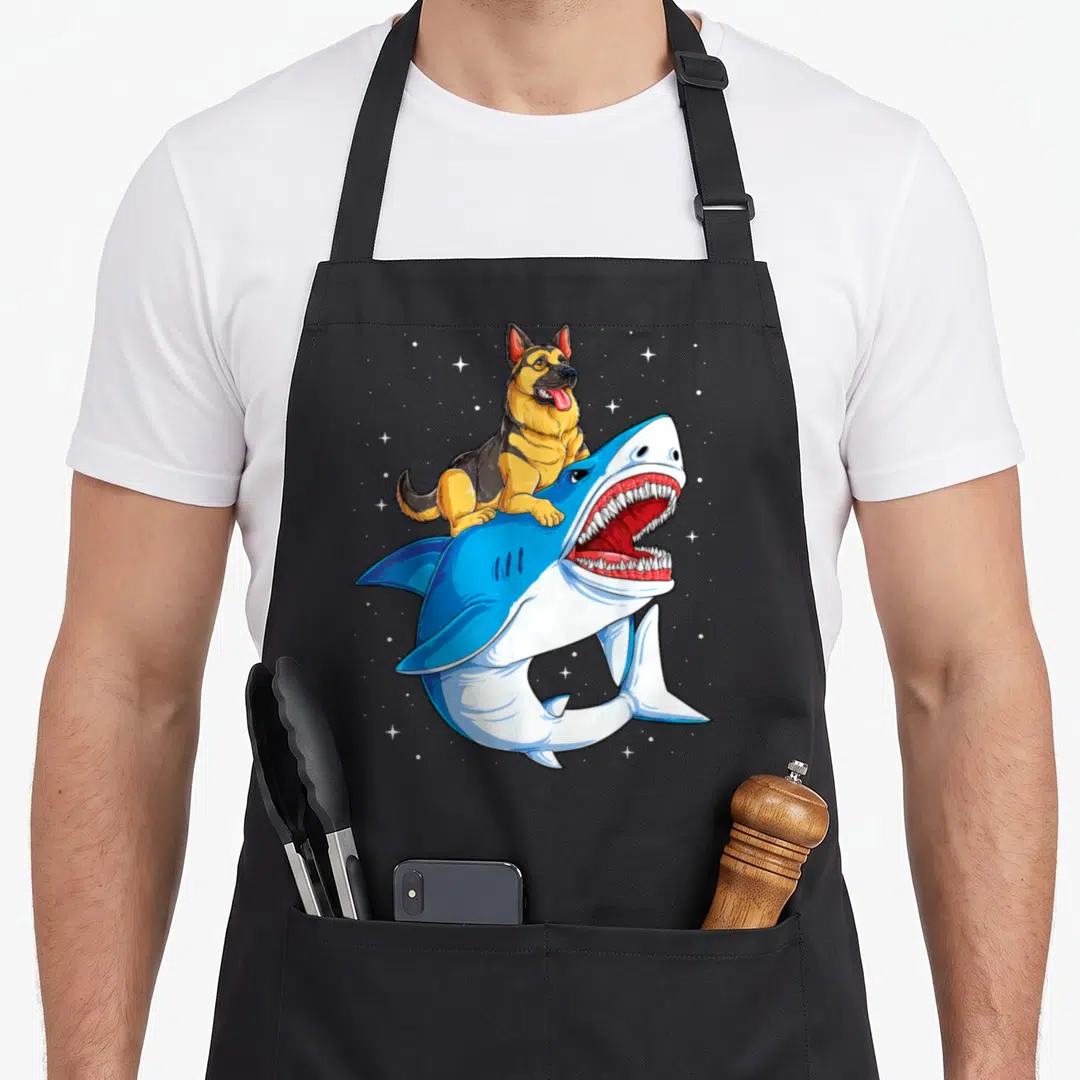 Shark german apron - Cartoon German Shepherd sitting on leaping blue shark with white stars — shown on a black cotton canvas apron against a white background