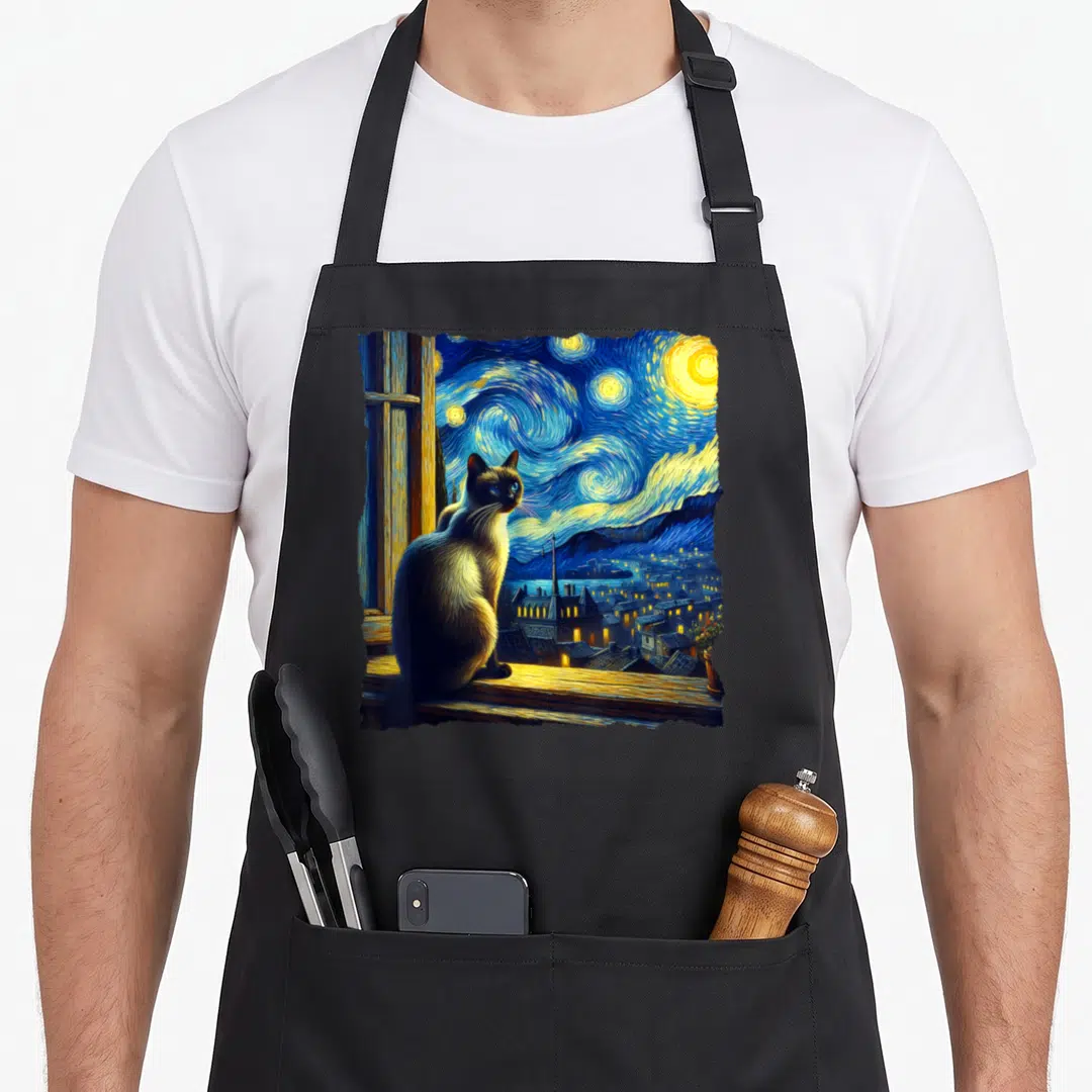 Night cute cat aprons - Siamese cat on windowsill overlooking swirling blue and yellow starry night sky over town — shown on a black cotton canvas apron against a white background