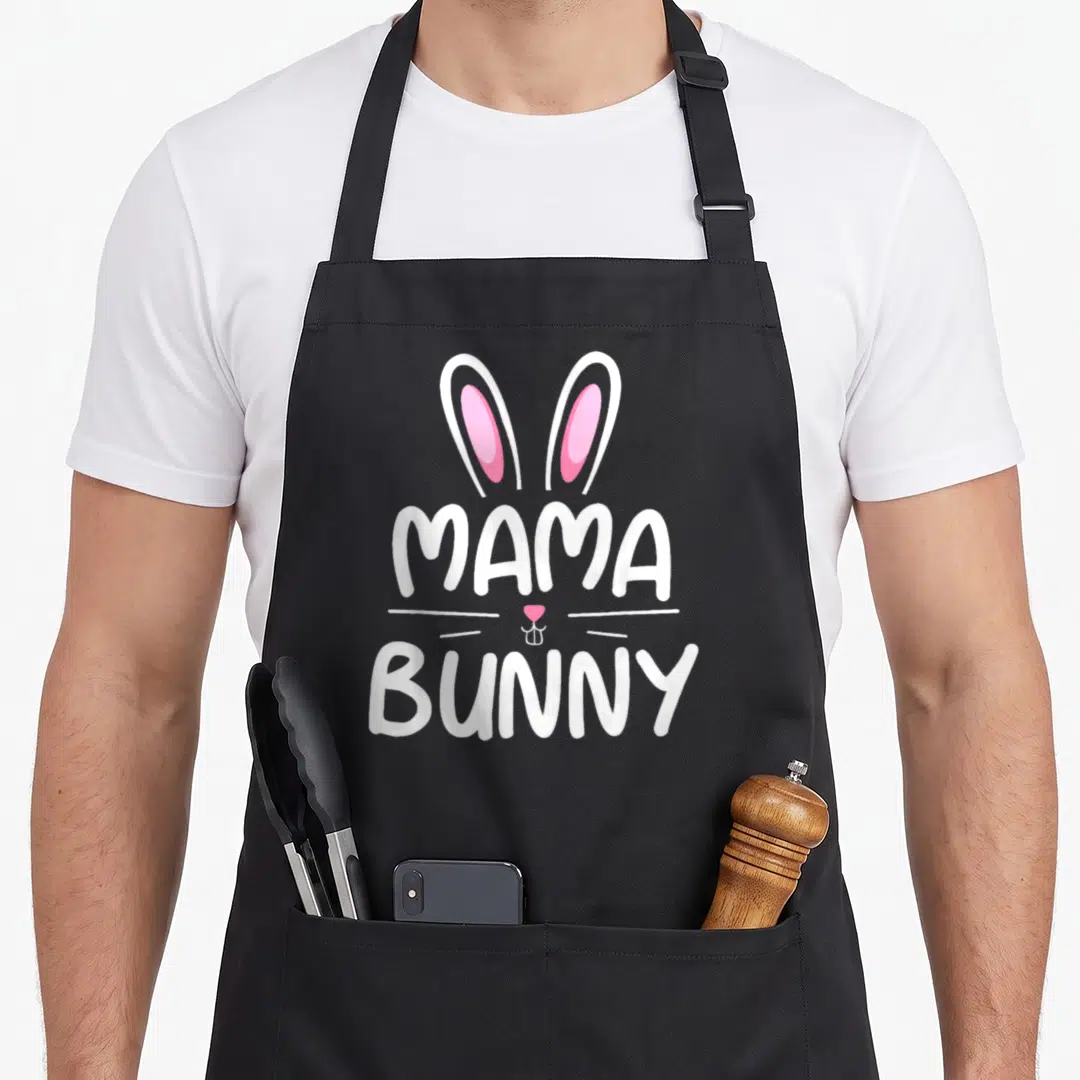Mama easter bunny aprons - Cartoon bunny face with white ears pink nose and MAMA BUNNY text — shown on a black cotton canvas apron against a white background