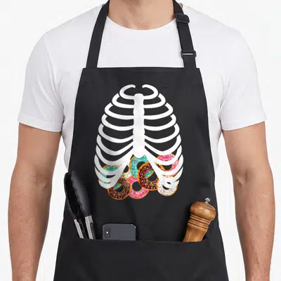 Food halloween apron - White cartoon ribcage filled with brown pink blue and white sprinkled donuts — shown on a black cotton canvas apron against a white background