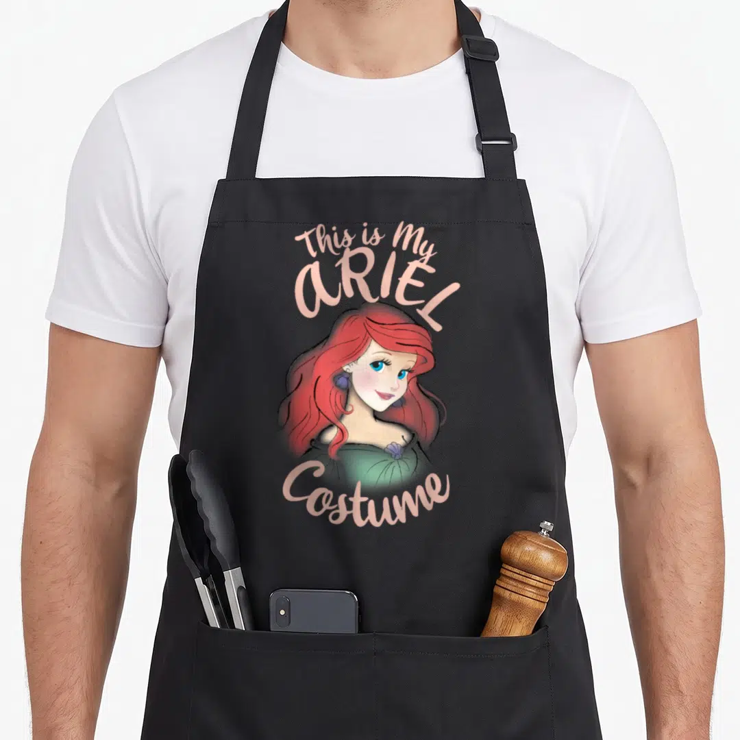 Ariel halloween apron - Cartoon Ariel portrait with This is My ARIEL Costume text in pink, red, and green — shown on a black cotton canvas apron against a white background