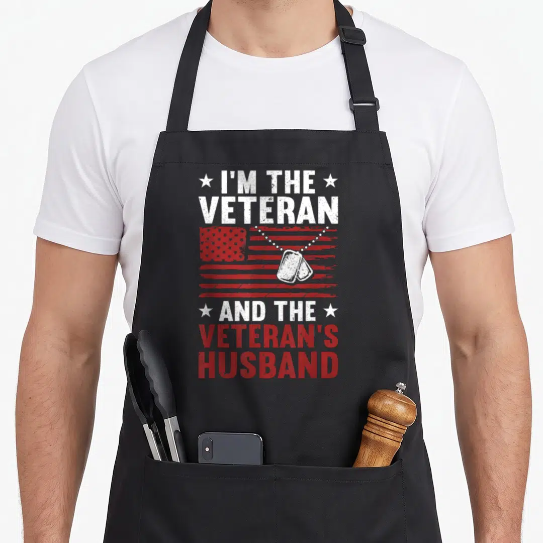 Vintage veteran best husband apron - Distressed red white USA flag with dog tags and stacked text I'm The Veteran — shown on a black cotton canvas apron against a white background