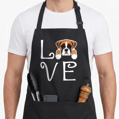 Puppy boxer dog apron - Cartoon Boxer puppy head and paws forming the O in white LOVE text — shown on a black cotton canvas apron against a white background