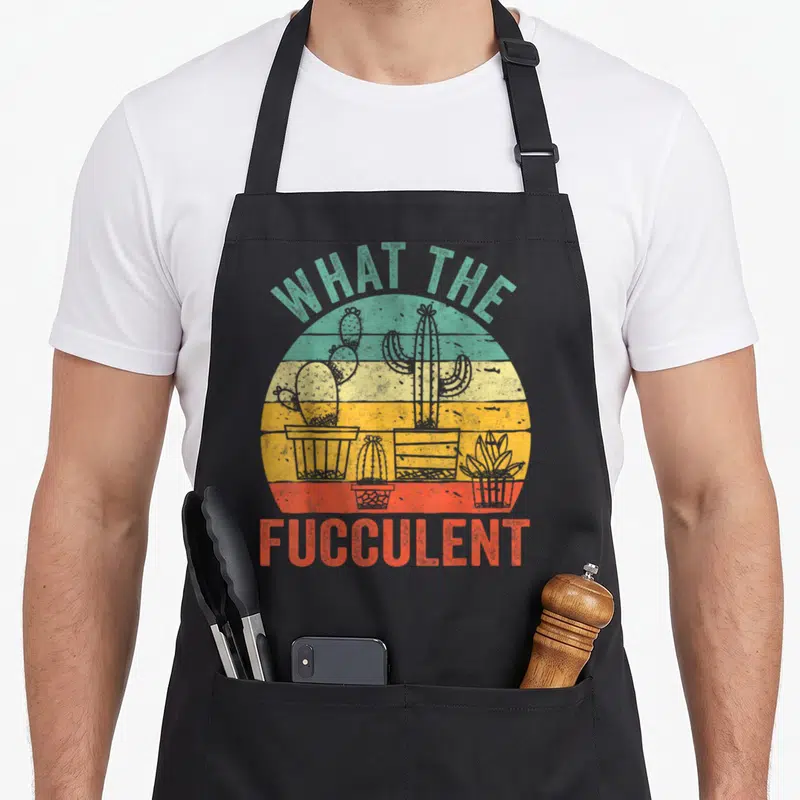 Fucculent succulent cactus apron - Retro sun with three potted cacti and text WHAT THE FUCCULENT in teal and red — shown on a black cotton canvas apron against a white background