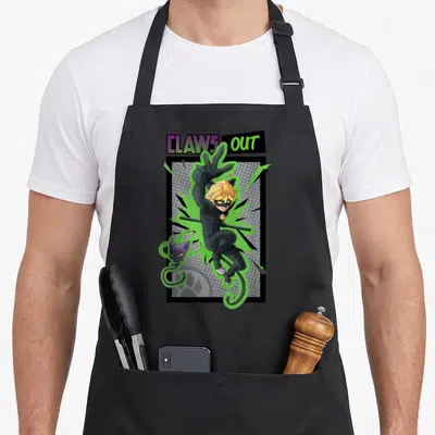 Noir cat apron - CLAWS OUT text above cartoon character in black suit with green energy and small purple cat — shown on a black cotton canvas apron against a white background