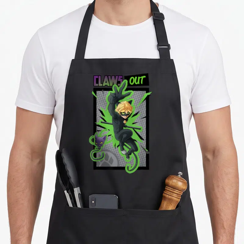 Noir cat apron - CLAWS OUT text above cartoon character in black suit with green energy and small purple cat — shown on a black cotton canvas apron against a white background