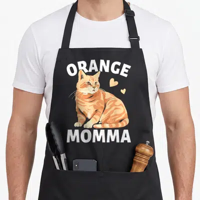 Momma cat in an apron - Orange tabby cat illustration between white ORANGE and MOMMA text with two small hearts — shown on a black cotton canvas apron against a white background