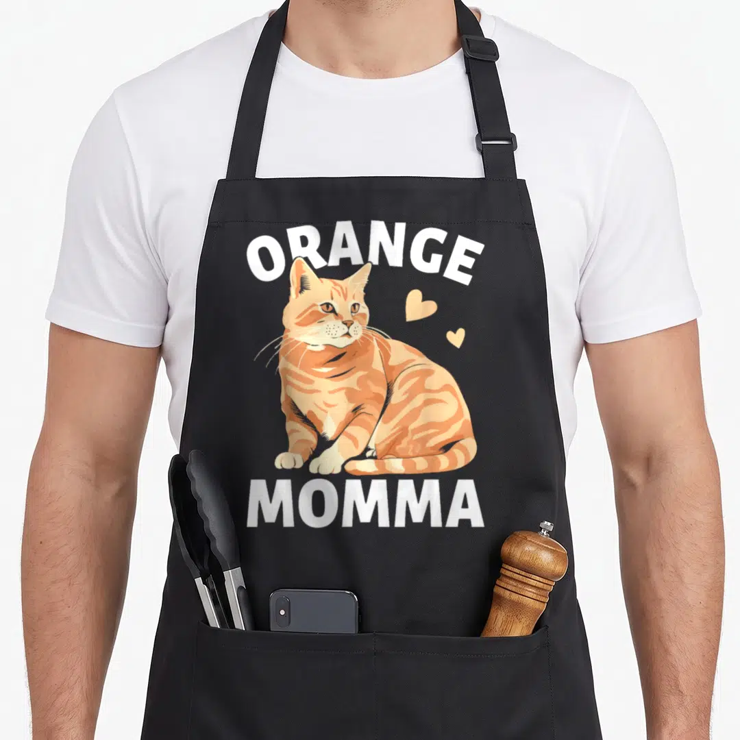 Momma cat in an apron - Orange tabby cat illustration between white ORANGE and MOMMA text with two small hearts — shown on a black cotton canvas apron against a white background