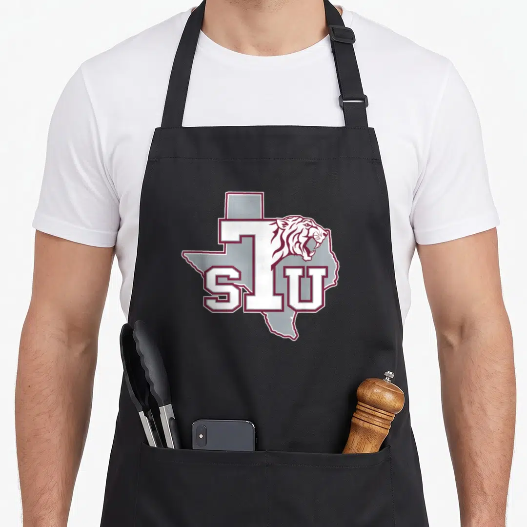 Authentic southern aprons - Maroon white STU letters tiger head grey Texas state outline cartoon graphic — shown on a black cotton canvas apron against a white background