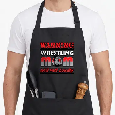 Retro wrestling apron - WARNING WRESTLING MOM Will Yell Loudly text with vintage woman illustration in red white black — shown on a black cotton canvas apron against a white background