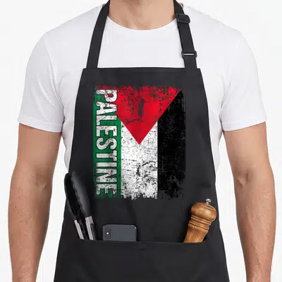 Cute flag palestine apron - Distressed Palestine flag print with vertical white text over a green stripe and red — shown on a black cotton canvas apron against a white background