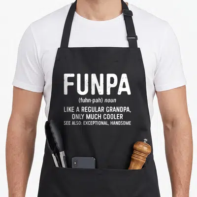 Funpa grandpa apron - White dictionary definition text reading funpa like a regular grandpa only much cooler — shown on a black cotton canvas apron against a white background
