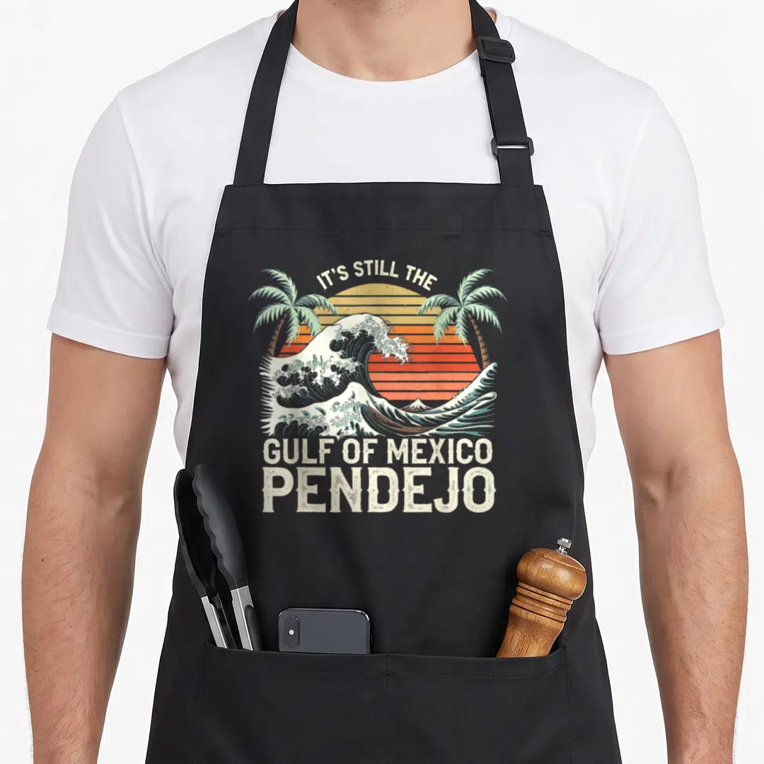 Gulf spanish aprons - Retro wave and palm trees with text IT'S STILL THE GULF OF MEXICO PENDEJO — shown on a black cotton canvas apron against a white background
