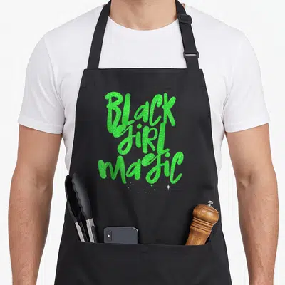 Magic lime green apron - Stacked green glitter text reading Black Girl Magic with small white stars below — shown on a black cotton canvas apron against a white background