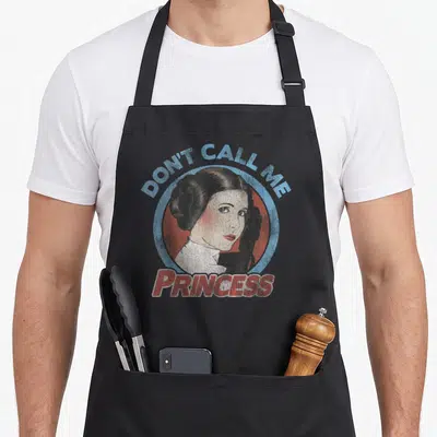 Call portrait princess apron - Retro portrait of a woman in a circle with text DON'T CALL ME PRINCESS in blue and red — shown on a black cotton canvas apron against a white background