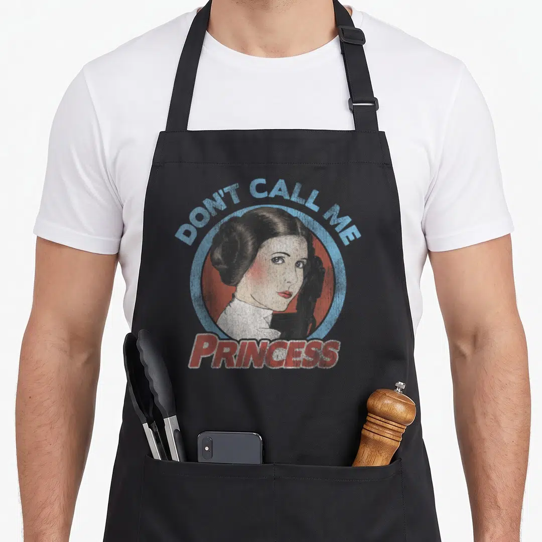 Call portrait princess apron - Retro portrait of a woman in a circle with text DON'T CALL ME PRINCESS in blue and red — shown on a black cotton canvas apron against a white background