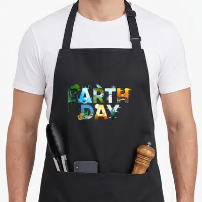 Environmental tree apron - Stacked EARTH DAY text filled with nature scenes in blue, green, yellow, and orange — shown on a black cotton canvas apron against a white background
