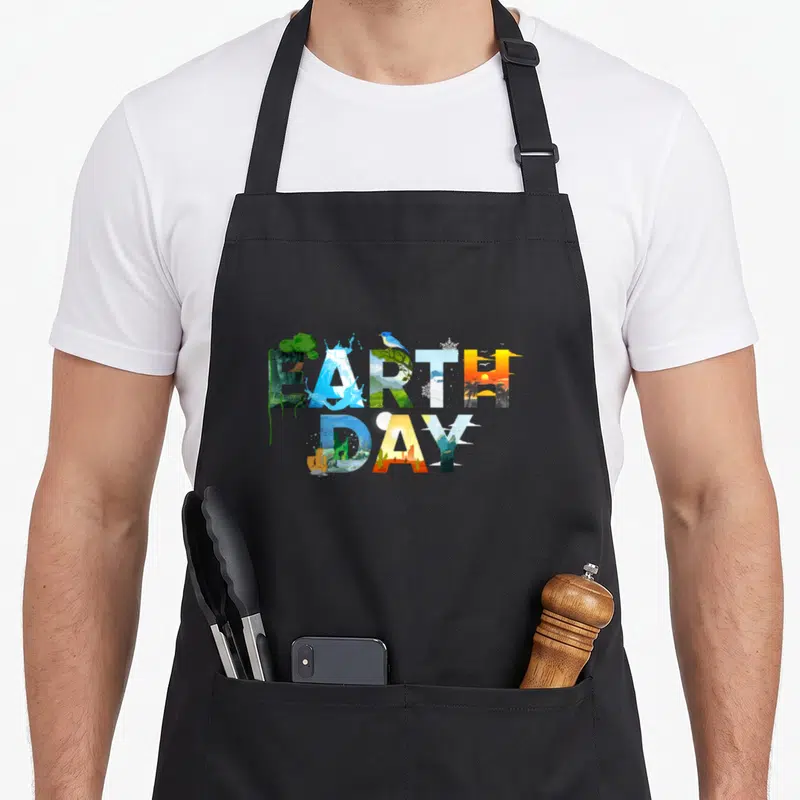 Environmental tree apron - Stacked EARTH DAY text filled with nature scenes in blue, green, yellow, and orange — shown on a black cotton canvas apron against a white background