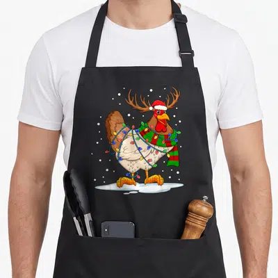 Chicken reindeer apron - Cartoon brown turkey with antlers, santa hat, striped scarf, and Christmas lights standing — shown on a black cotton canvas apron against a white background