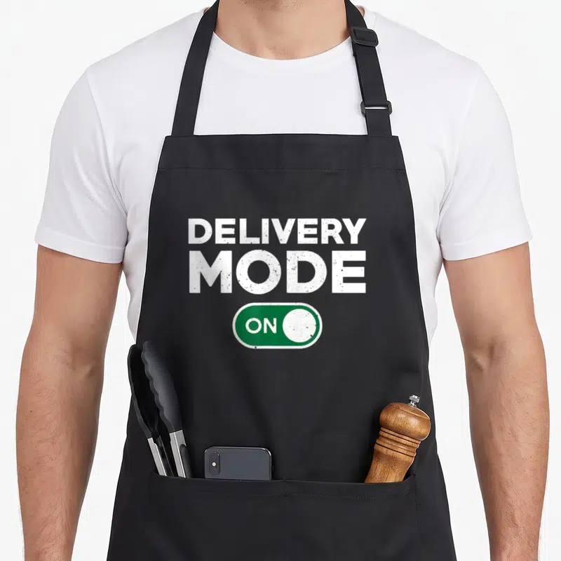 Driver delivery dad apron - Distressed white text DELIVERY MODE ON above a green toggle switch — shown on a black cotton canvas apron against a white background