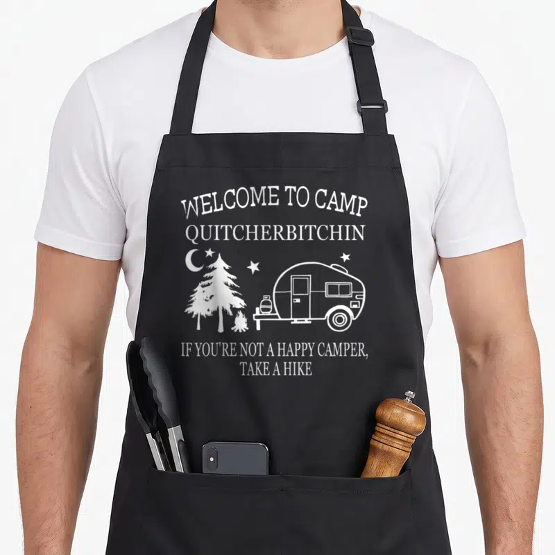 Welcome camping apron - White camper trailer, pine tree, campfire, moon and stars with sarcastic camping text — shown on a black cotton canvas apron against a white background