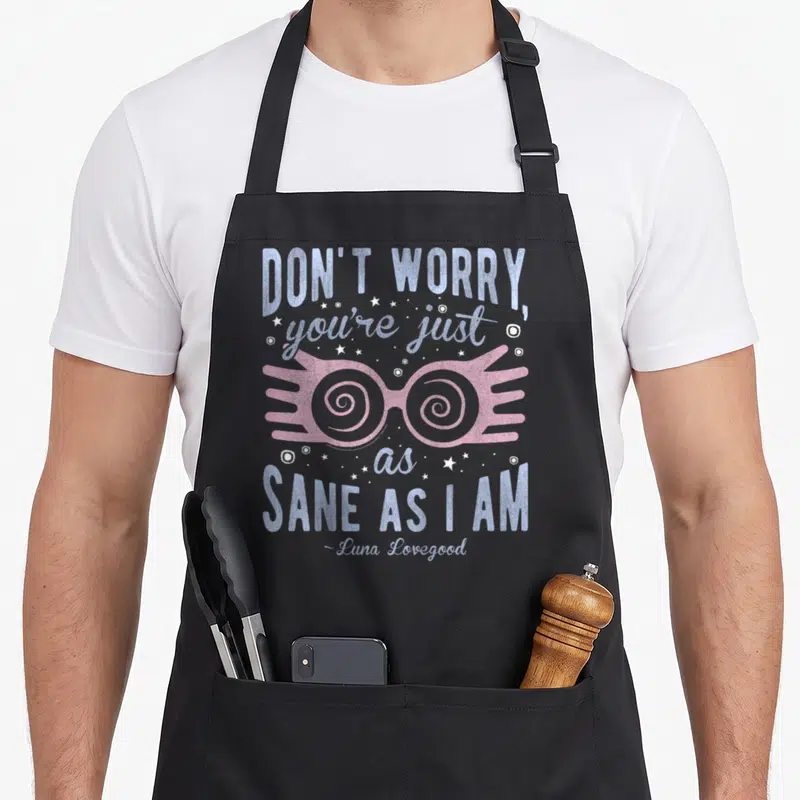 Sane a's aprons - Pink spiral spectacles with blue and white text DON'T WORRY you're just as SANE AS I AM surrounded — shown on a black cotton canvas apron against a white background