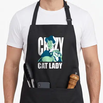 Tremaine crazy cat lady apron - Cartoon woman holding a cat with text CRAZY CAT LADY in blue, mint, and white — shown on a black cotton canvas apron against a white background