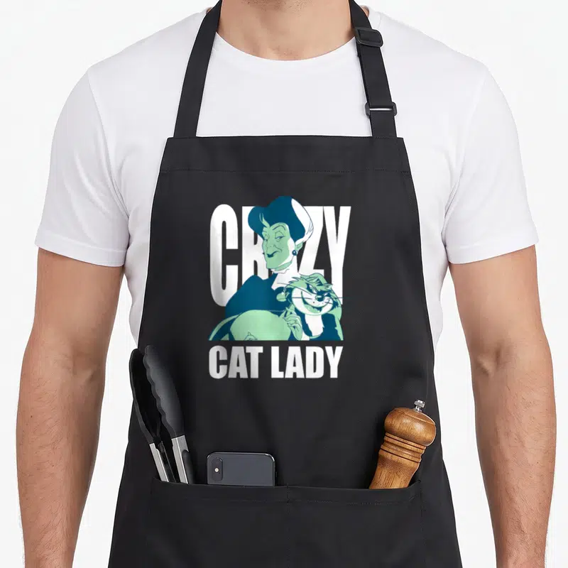 Tremaine crazy cat lady apron - Cartoon woman holding a cat with text CRAZY CAT LADY in blue, mint, and white — shown on a black cotton canvas apron against a white background