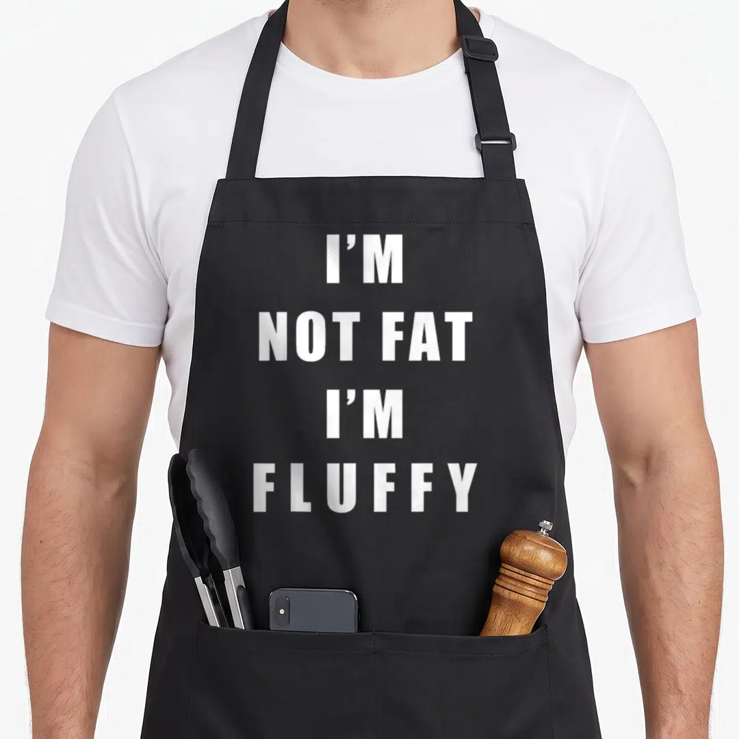 Fluffy fat man in apron - White stacked text I'M NOT FAT I'M FLUFFY on black bib apron — shown on a black cotton canvas apron against a white background