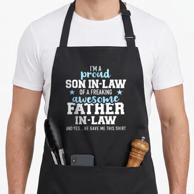 Funny proud father son apron - White and blue text reading I'm a proud son in law of a freaking awesome father in law — shown on a black cotton canvas apron against a white background