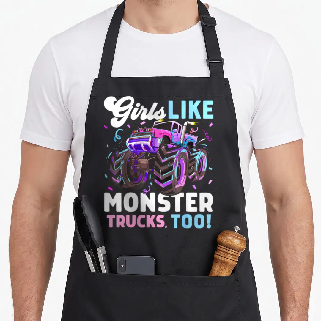 Vintage monster truck aprons - Pink purple blue monster truck cartoon with Girls LIKE MONSTER TRUCKS TOO text — shown on a black cotton canvas apron against a white background
