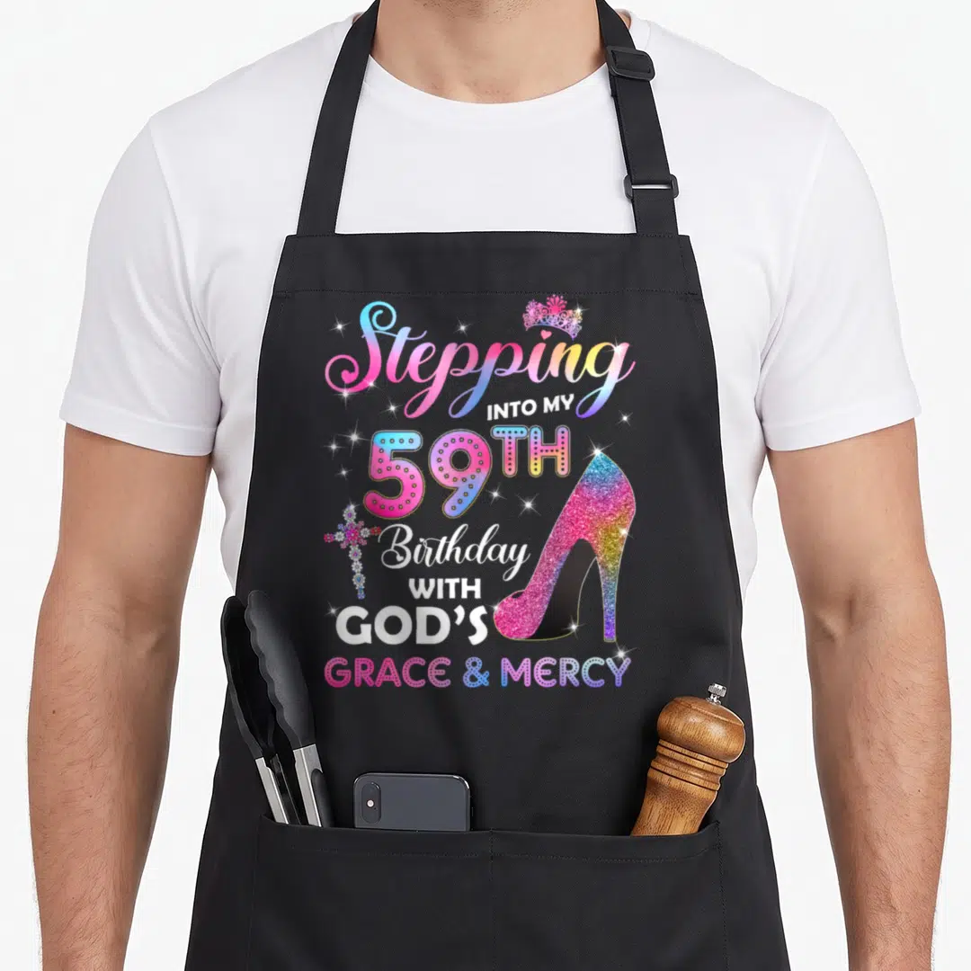 Stepping 59th birthday apron - Rainbow gradient text with glittery high heel, crown, and cross celebrating 59th birthday — shown on a black cotton canvas apron against a white background
