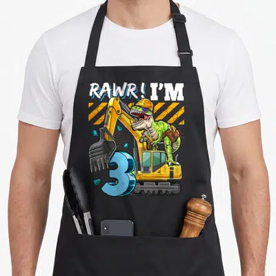 Rex construction apron - Green T-Rex in yellow excavator with blue number 3 and orange stripes — shown on a black cotton canvas apron against a white background