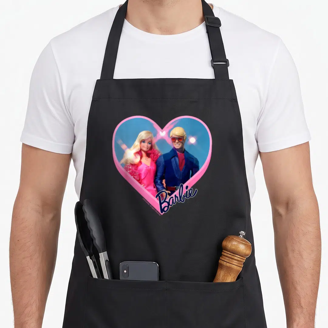 Ken general apron - Photo of Barbie and Ken inside pink heart border with blue background — shown on a black cotton canvas apron against a white background