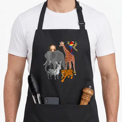 Wildlife birthday apron - Cartoon elephant zebra tiger giraffe monkey and parrot in grey orange brown white and black — shown on a black cotton canvas apron against a white background