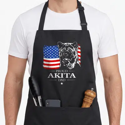 Akita american flag apron - Distressed US flag behind Akita head with Proud Akita Dad text and small star — shown on a black cotton canvas apron against a white background
