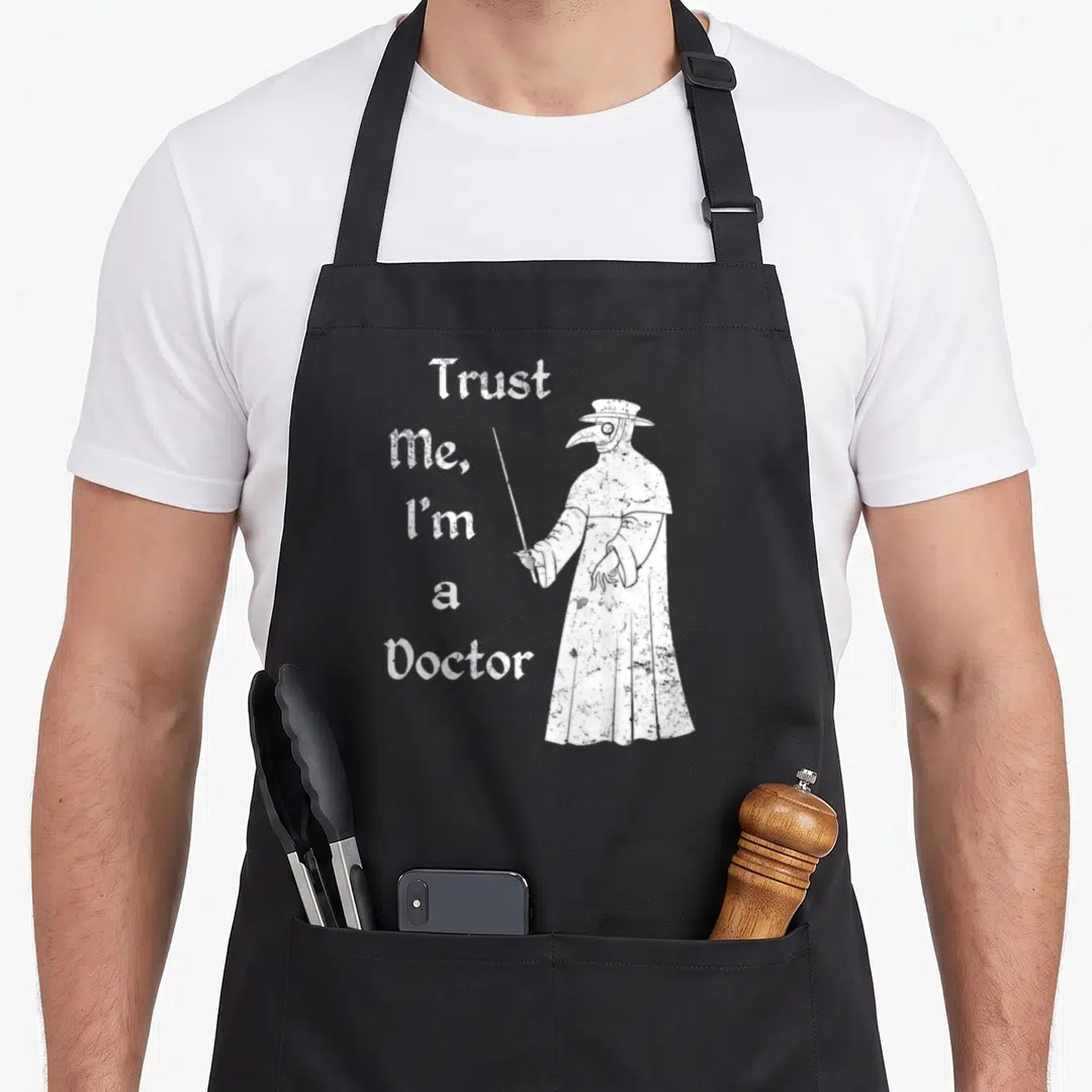 Trust plague doctor apron - White distressed text Trust Me I'm a Doctor beside a plague doctor figure pointing a cane — shown on a black cotton canvas apron against a white background