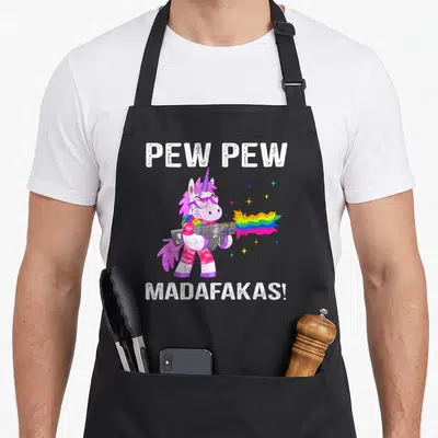 Unicorn black cat aprons - Cartoon unicorn in pink and purple firing a rainbow beam with white text — shown on a black cotton canvas apron against a white background