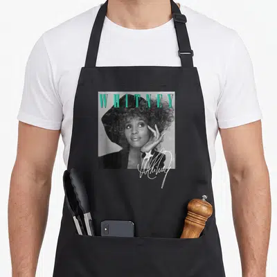 Whitney shooting apron - Grayscale woman in hat with teal WHITNEY text and white signature star — shown on a black cotton canvas apron against a white background