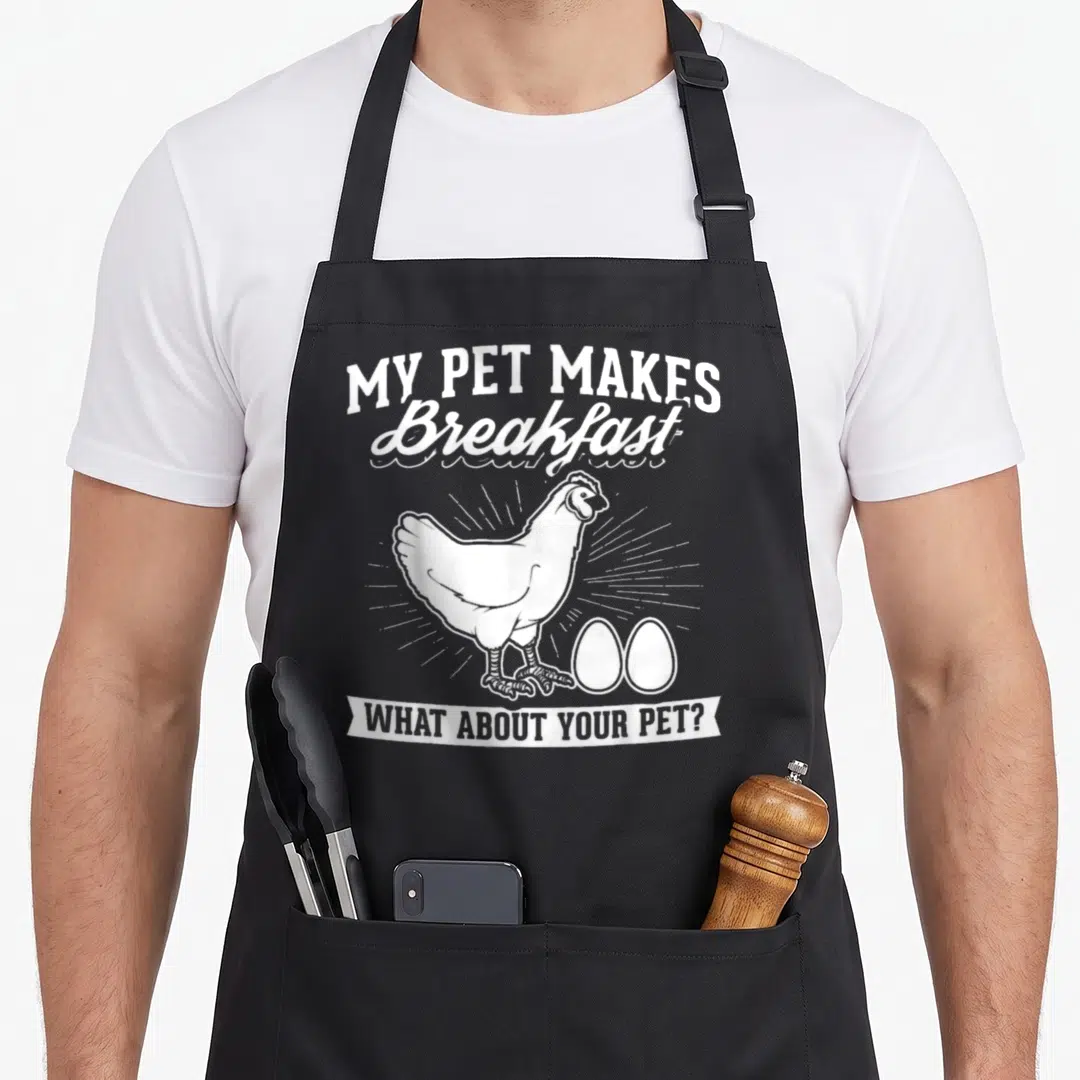 Macht pet apron - White cartoon chicken and two eggs with breakfast text on black background — shown on a black cotton canvas apron against a white background