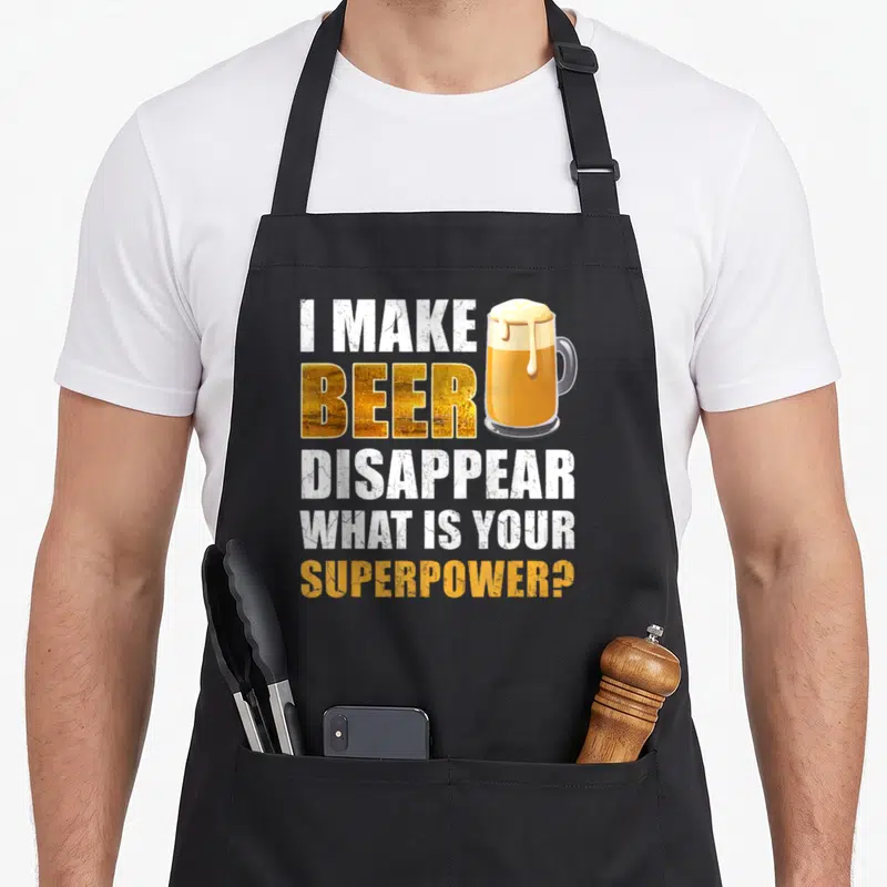 Beer gag aprons - I Make Beer Disappear text next to a gold mug with dripping foam — shown on a black cotton canvas apron against a white background