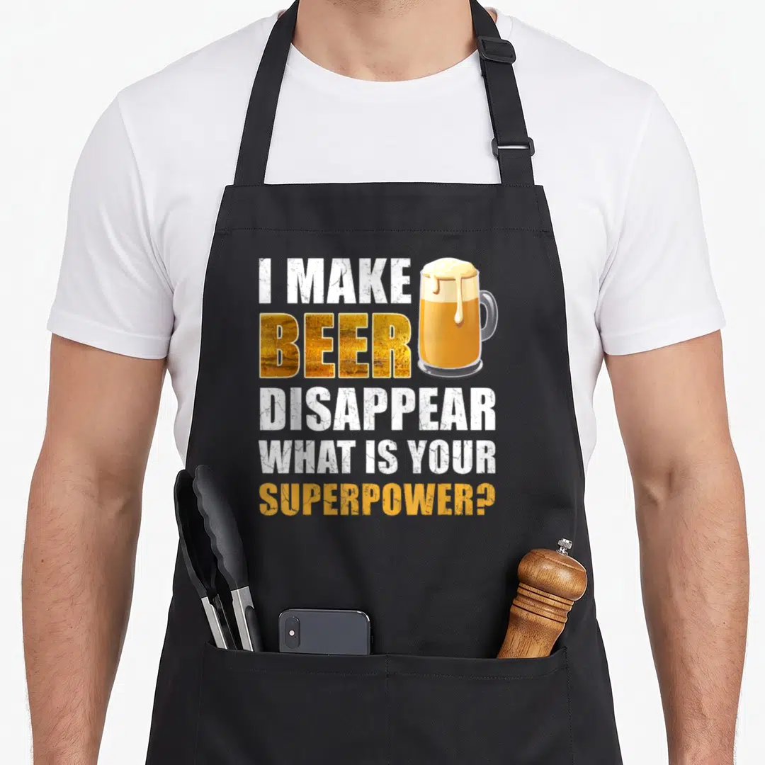 Beer gag aprons - I Make Beer Disappear text next to a gold mug with dripping foam — shown on a black cotton canvas apron against a white background