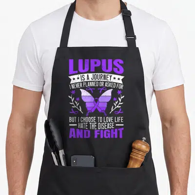 Sle butterfly apron - Purple butterfly with awareness ribbon and stacked lupus journey text flanked by floral branches — shown on a black cotton canvas apron against a white background
