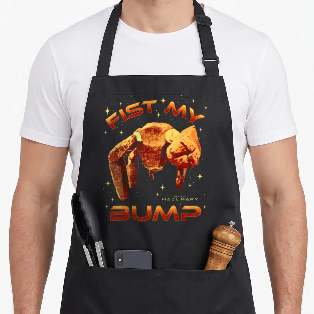 Project fist bump apron - Rocky alien hand with FIST MY BUMP text and stars in orange yellow white — shown on a black cotton canvas apron against a white background