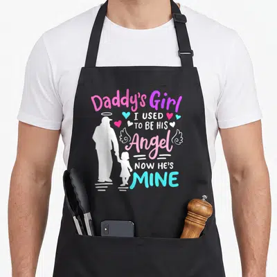 Daddy angels and aprons - White father daughter silhouette with pink blue purple text reading I used to be his angel — shown on a black cotton canvas apron against a white background