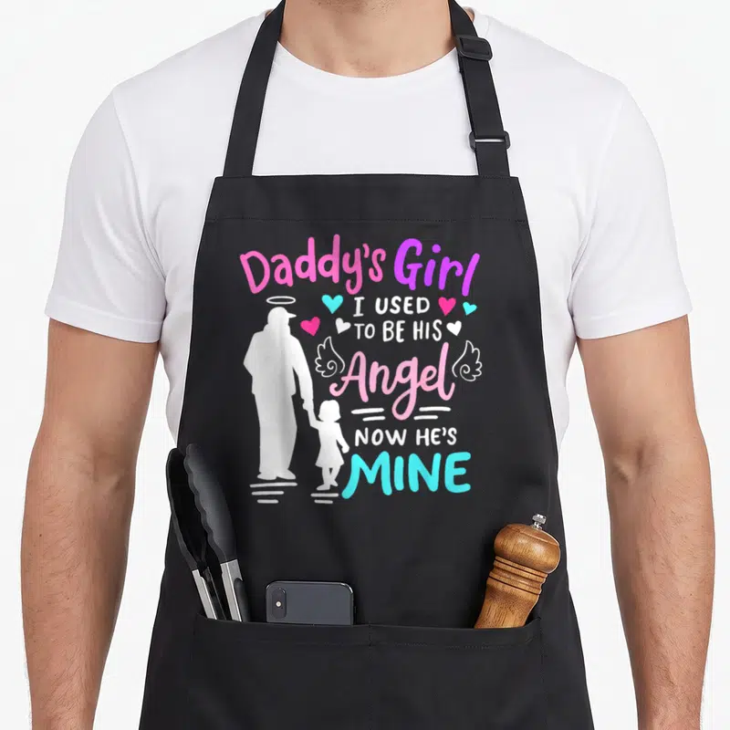 Daddy angels and aprons - White father daughter silhouette with pink blue purple text reading I used to be his angel — shown on a black cotton canvas apron against a white background