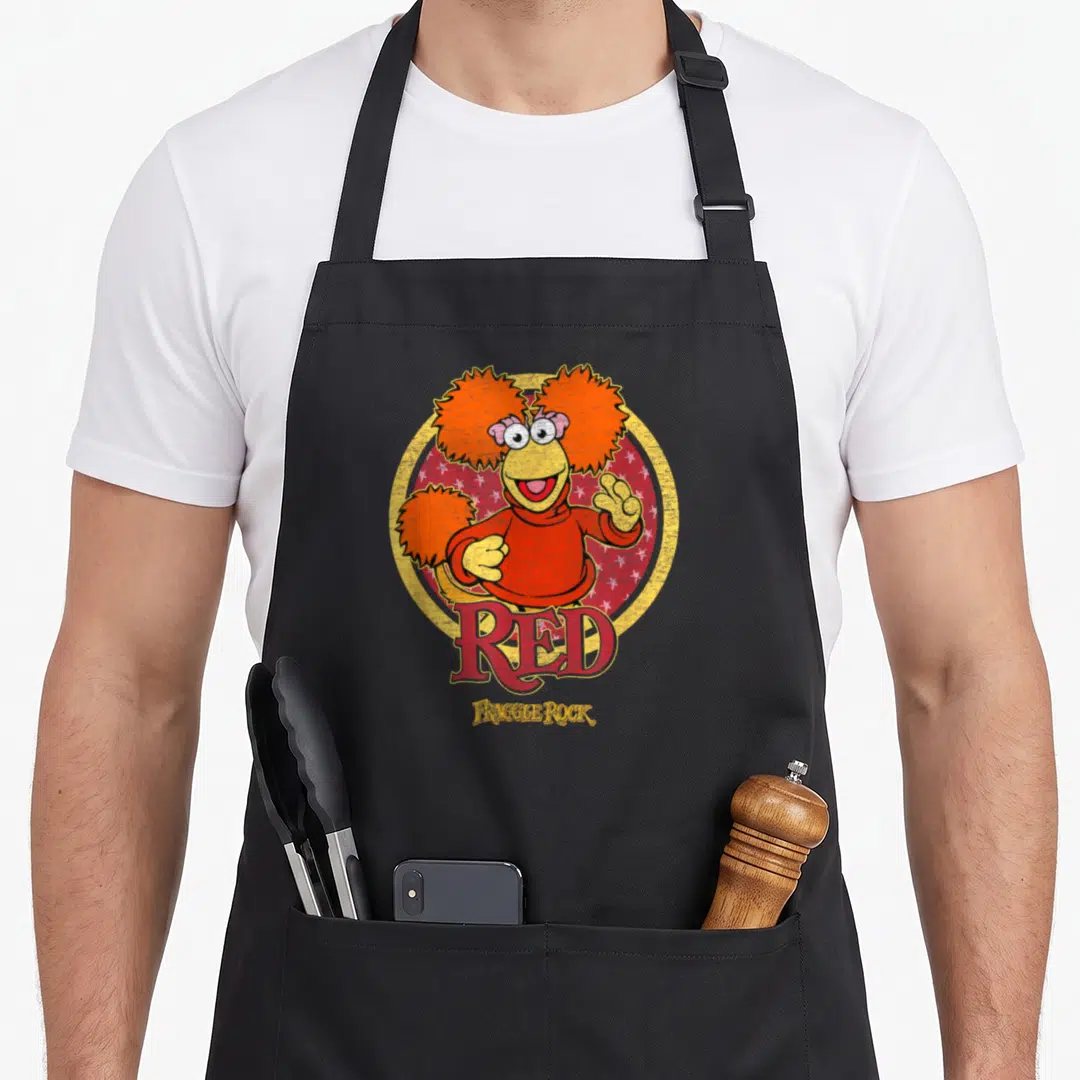 Fraggle red rocks apron - Cartoon Fraggle Red character in yellow circle with white stars and red text — shown on a black cotton canvas apron against a white background