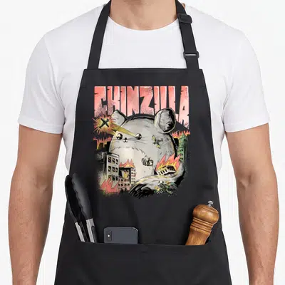Monster chinchilla lover apron - Giant grey chinchilla firing lasers at planes under pink CHINZILLA text — shown on a black cotton canvas apron against a white background