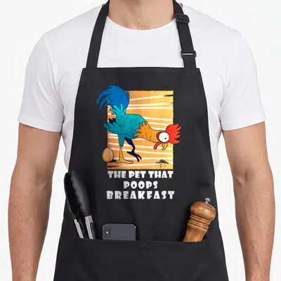 Poop breakfast chicken apron - Cartoon rooster with egg and droppings above white text THE PET THAT, POOPS, BREAKFAST — shown on a black cotton canvas apron against a white background
